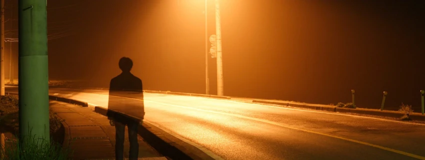 Ein Mann steht im Licht einer Straßenlaterne. Durch ihn schimmert die Straße.