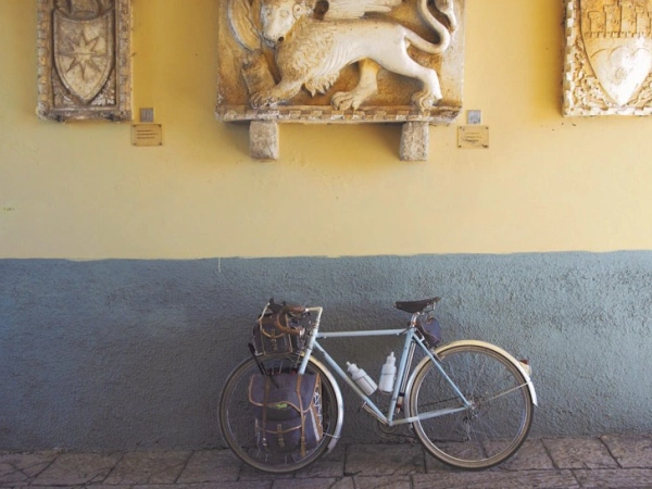 Ein Fahrrad lehnt an einer Wand, die mit Skulpturen, von Wappen und einem Löwen, geschmückt ist