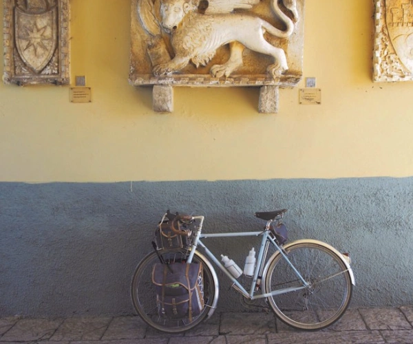 Ein Fahrrad lehnt an einer Wand, die mit Skulpturen, von Wappen und einem Löwen, geschmückt ist