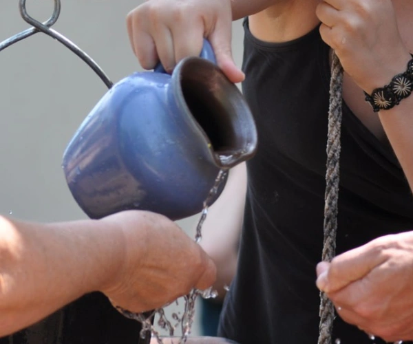 Ein Wasserkrug wird über offenen Händen ausgegossen.