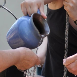 Ein Wasserkrug wird über offenen Händen ausgegossen.
