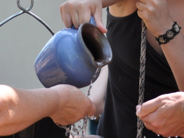 Ein Wasserkrug wird über offenen Händen ausgegossen.