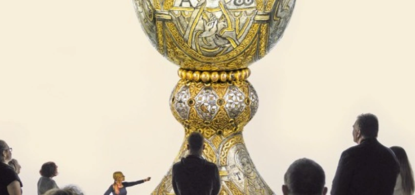 Menschen sind um einen großen goldenen Kelch versammelt.