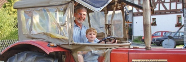 Ein Mann und ein Kind sitzen in einem Roten Traktor am Lenkrad.