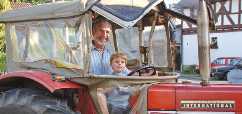 Ein Mann und ein Kind sitzen in einem Roten Traktor am Lenkrad.