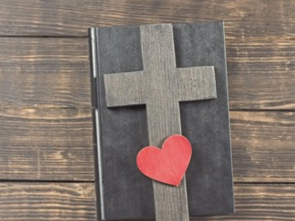 Auf einem, in Leder gebundenem, Buch liegt ein Holzkreuz und ein Herz.