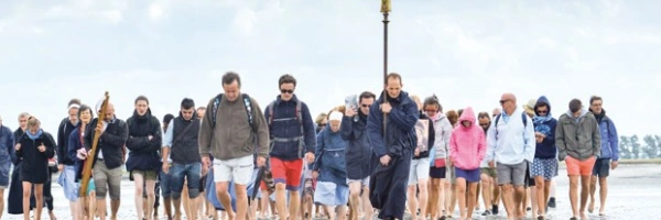 Eine Gruppe von Menschen läuft über den Strand auf den Beobachter zu. Sie tragen ein Kreuz.