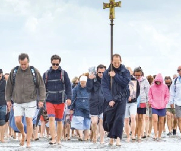 Eine Gruppe von Menschen läuft über den Strand auf den Beobachter zu. Sie tragen ein Kreuz.