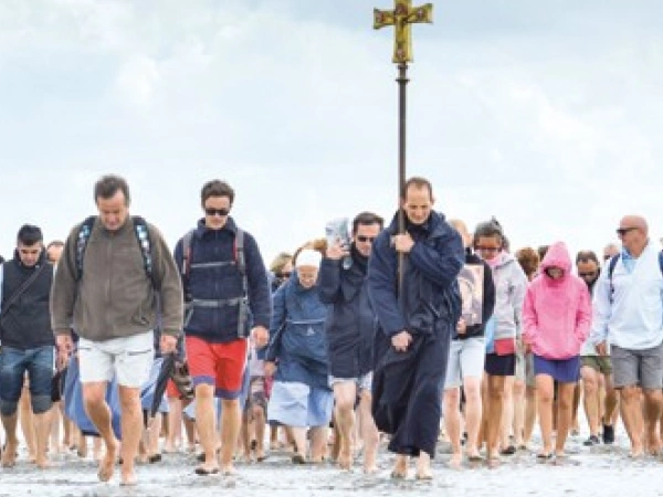 Eine Gruppe von Menschen läuft über den Strand auf den Beobachter zu. Sie tragen ein Kreuz.