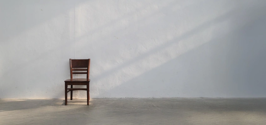 Mit dem Körper beten. Eine Anleitung. Bild eines Stuhls an der Wand in einem leeren Raum.
