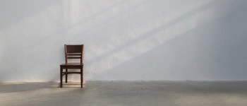 Mit dem Körper beten. Eine Anleitung. Bild eines Stuhls an der Wand in einem leeren Raum.