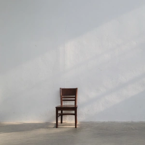 Mit dem Körper beten. Eine Anleitung. Bild eines Stuhls an der Wand in einem leeren Raum.