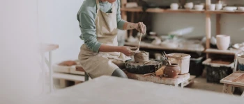 Eine Frau sitzt in der Werkstatt und töpfert.