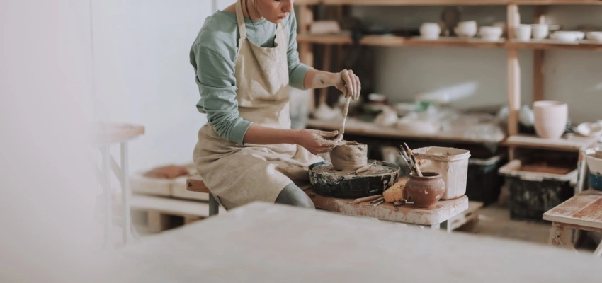 Eine Frau sitzt in der Werkstatt und töpfert.