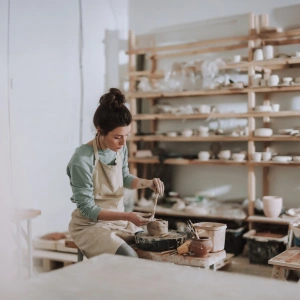Eine Frau sitzt in der Werkstatt und töpfert.