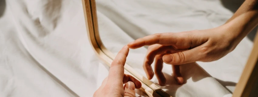 Eine Hand berührt ihr Spiegelbild, in einem Spiegel.