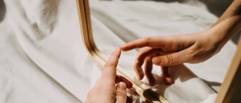 Eine Hand berührt ihr Spiegelbild, in einem Spiegel.