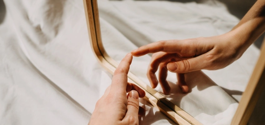 Eine Hand berührt ihr Spiegelbild, in einem Spiegel.
