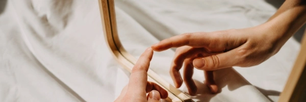 Eine Hand berührt ihr Spiegelbild, in einem Spiegel.