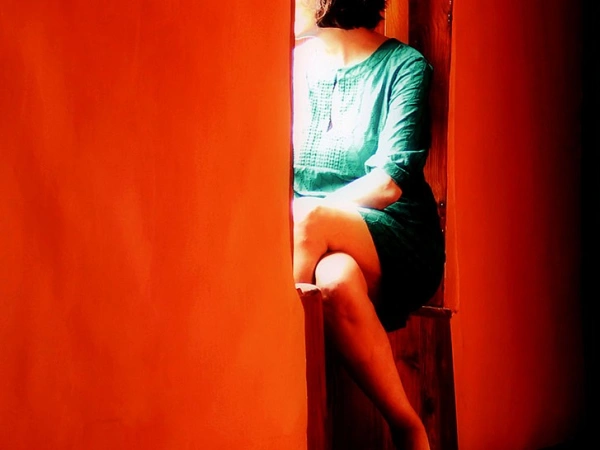 In einer roten Wand ist eine Sitznische eingelassen, darin sitzt eine zum Beobachter abgewandte Frau.