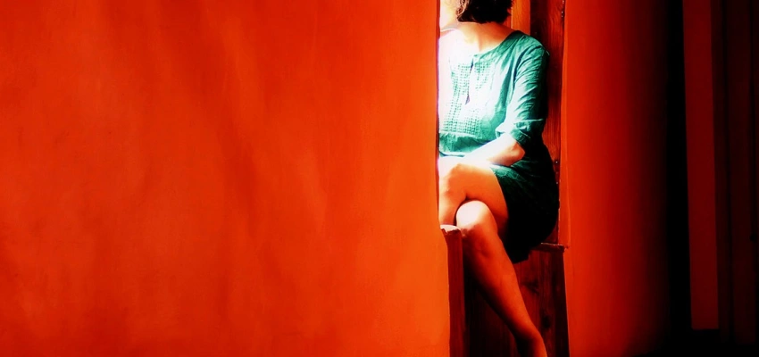 In einer roten Wand ist eine Sitznische eingelassen, darin sitzt eine zum Beobachter abgewandte Frau.