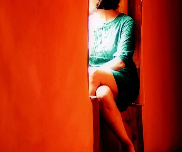 In einer roten Wand ist eine Sitznische eingelassen, darin sitzt eine zum Beobachter abgewandte Frau.
