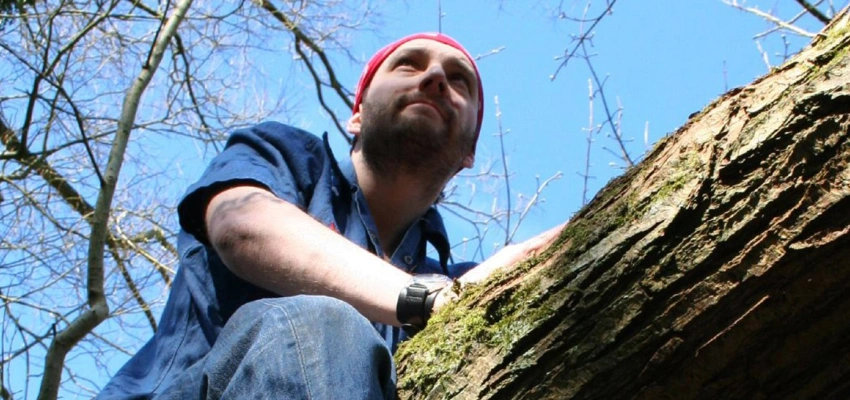 Ein Mann sitzt auf einem dicken Ast.