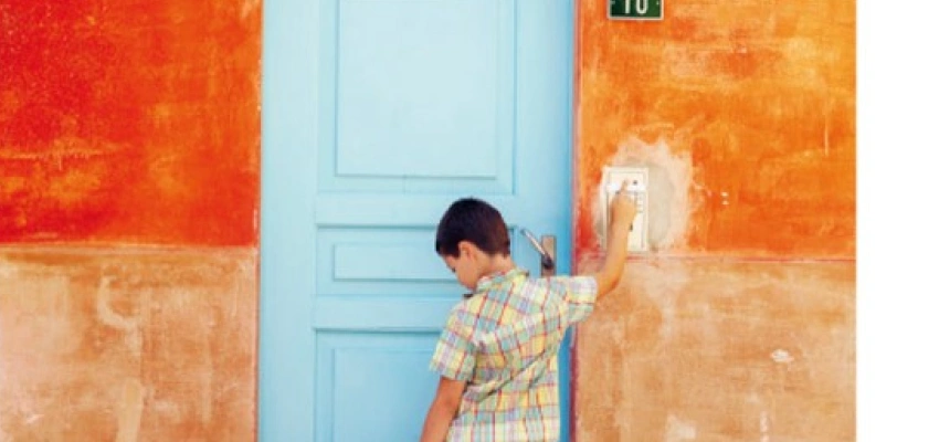 Ein Kind mit Koffer in der Hand klingelt an einer Haustür