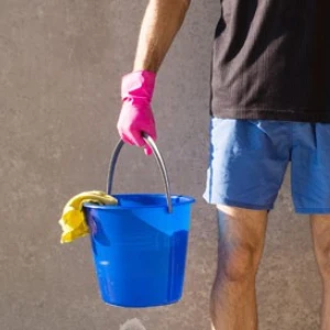Mensch in kurzer Hose und pinken Gummihandschuhen, mit Putzeimer und Besen in der Hand