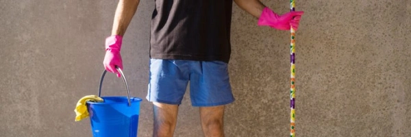 Mensch in kurzer Hose und pinken Gummihandschuhen, mit Putzeimer und Besen in der Hand