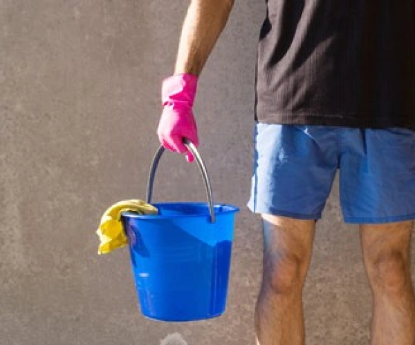 Mensch in kurzer Hose und pinken Gummihandschuhen, mit Putzeimer und Besen in der Hand