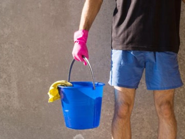 Mensch in kurzer Hose und pinken Gummihandschuhen, mit Putzeimer und Besen in der Hand