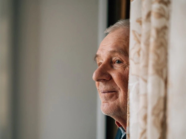 Alter Mann schaut hinter einer Gardine hervor in die Ferne