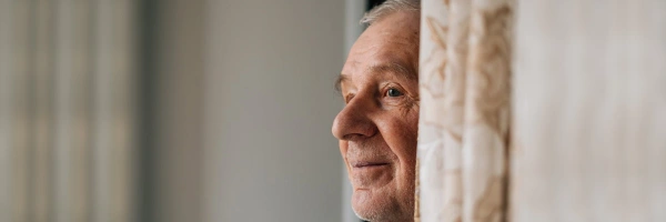 Alter Mann schaut hinter einer Gardine hervor in die Ferne