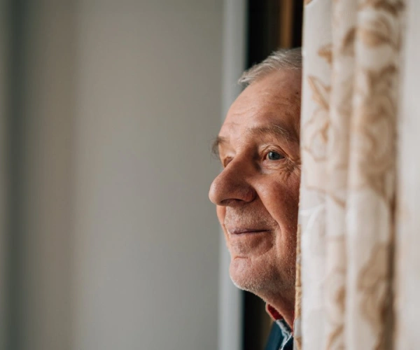 Alter Mann schaut hinter einer Gardine hervor in die Ferne