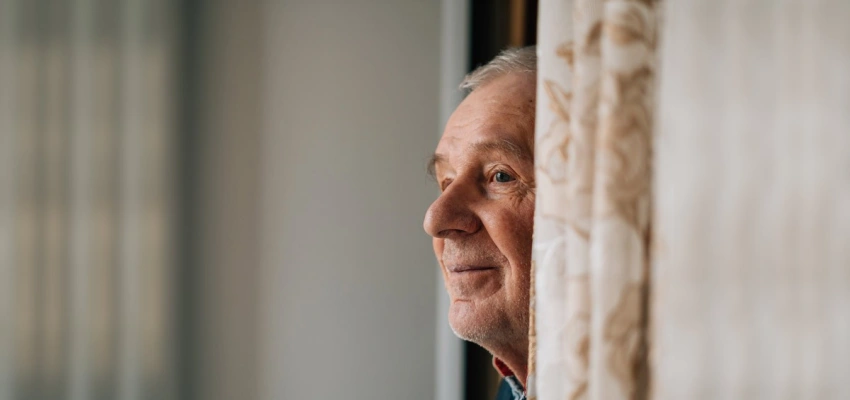 Alter Mann schaut hinter einer Gardine hervor in die Ferne