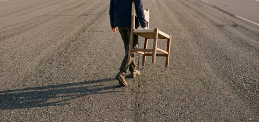 Mensch trägt einen leeren Stuhl auf einsamer Straße