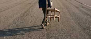 Mensch trägt einen leeren Stuhl auf einsamer Straße