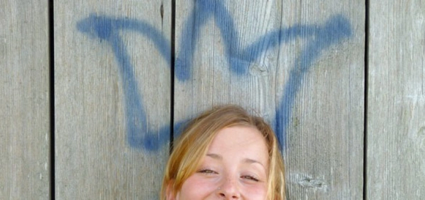 lächelnde Frau vor einer Bretterwand mit Graffiti-Krone