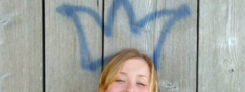 lächelnde Frau vor einer Bretterwand mit Graffiti-Krone