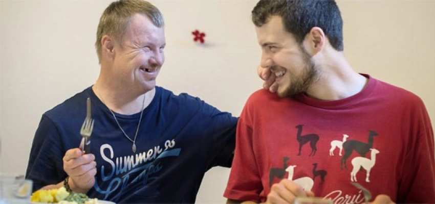 zwei sitzende Menschen grinsen sich herzlich an