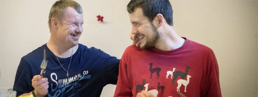 zwei sitzende Menschen grinsen sich herzlich an