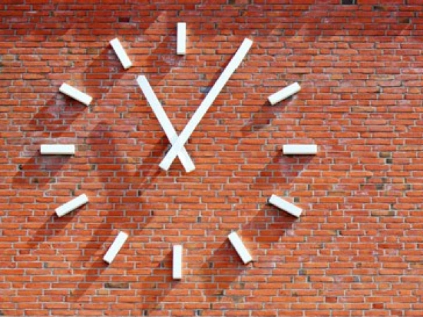 Wie spät ist es in meinem Leben? Aufmerken. durchatmen. ausrichten. weitergehen. Bild einer Uhr an einer Ziegelsteinwand.