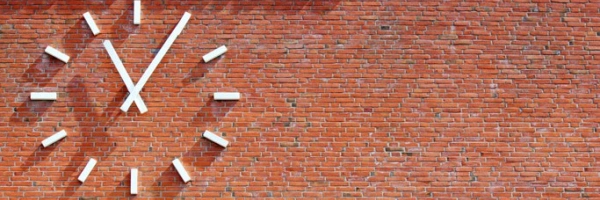 Wie spät ist es in meinem Leben? Aufmerken. durchatmen. ausrichten. weitergehen. Bild einer Uhr an einer Ziegelsteinwand.