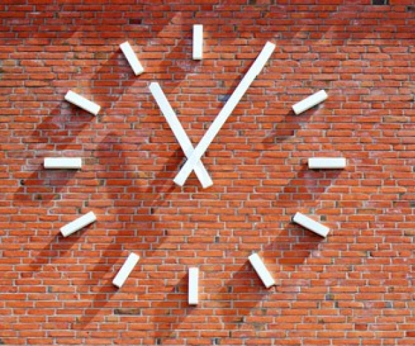 Wie spät ist es in meinem Leben? Aufmerken. durchatmen. ausrichten. weitergehen. Bild einer Uhr an einer Ziegelsteinwand.