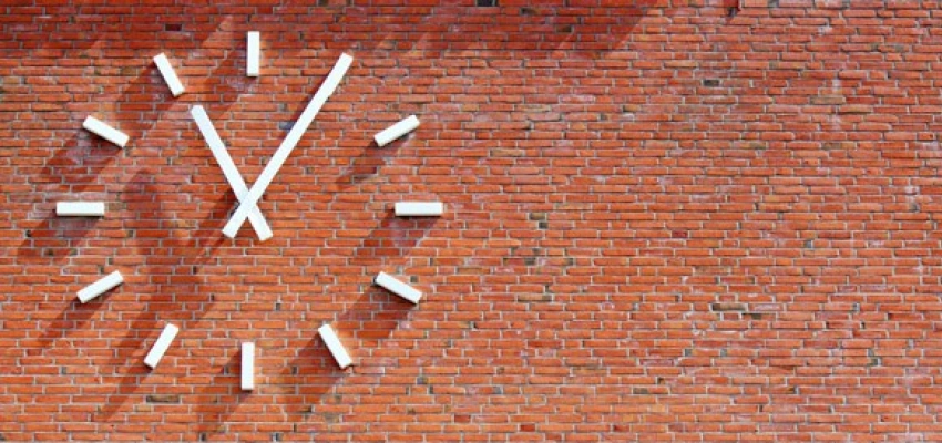 Wie spät ist es in meinem Leben? Aufmerken. durchatmen. ausrichten. weitergehen. Bild einer Uhr an einer Ziegelsteinwand.