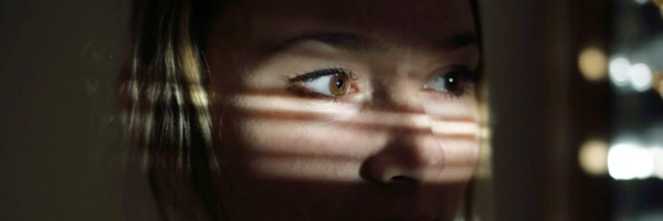 Frau in einem dunklen Raum schaut durch die Jalousien nach draußen