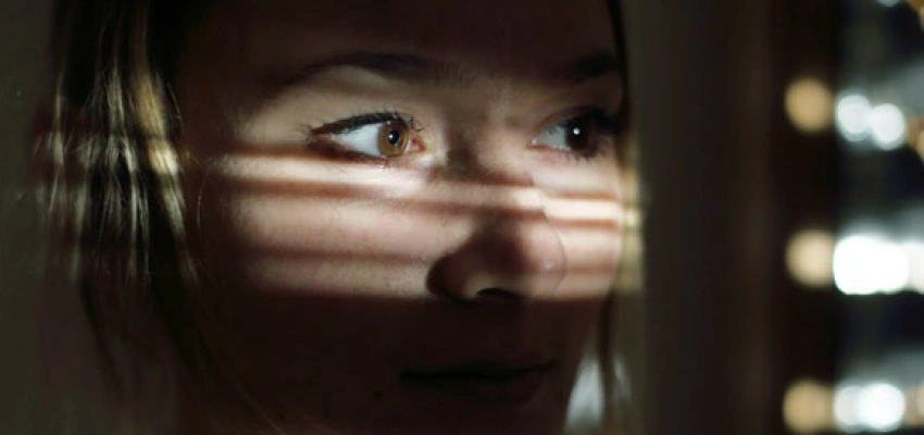 Frau in einem dunklen Raum schaut durch die Jalousien nach draußen