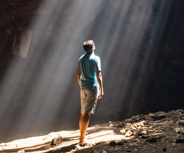Ein Mann steht in einer Höhle und blickt zu einem Spalt in der Decke, durch den die Sonnenstrahlen fallen.