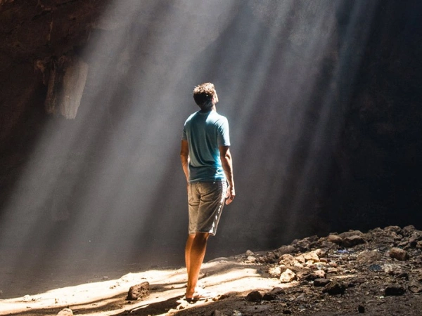 Ein Mann steht in einer Höhle und blickt zu einem Spalt in der Decke, durch den die Sonnenstrahlen fallen.